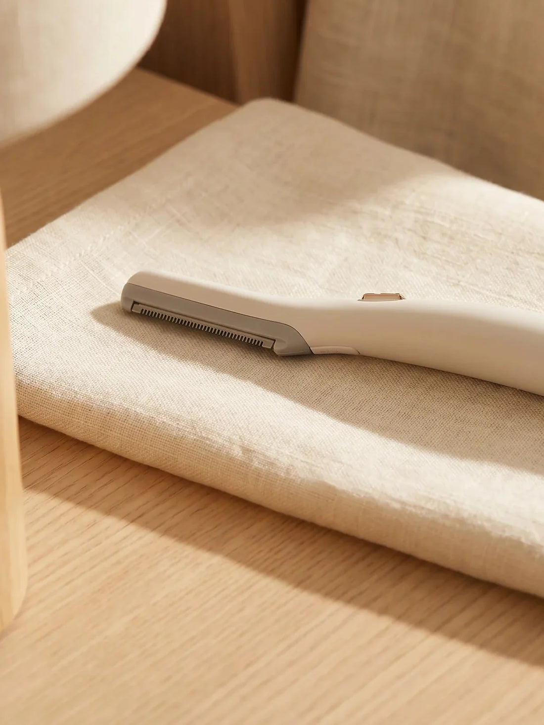 The Lumée LED facial trimmer resting on linen beside a gold ring